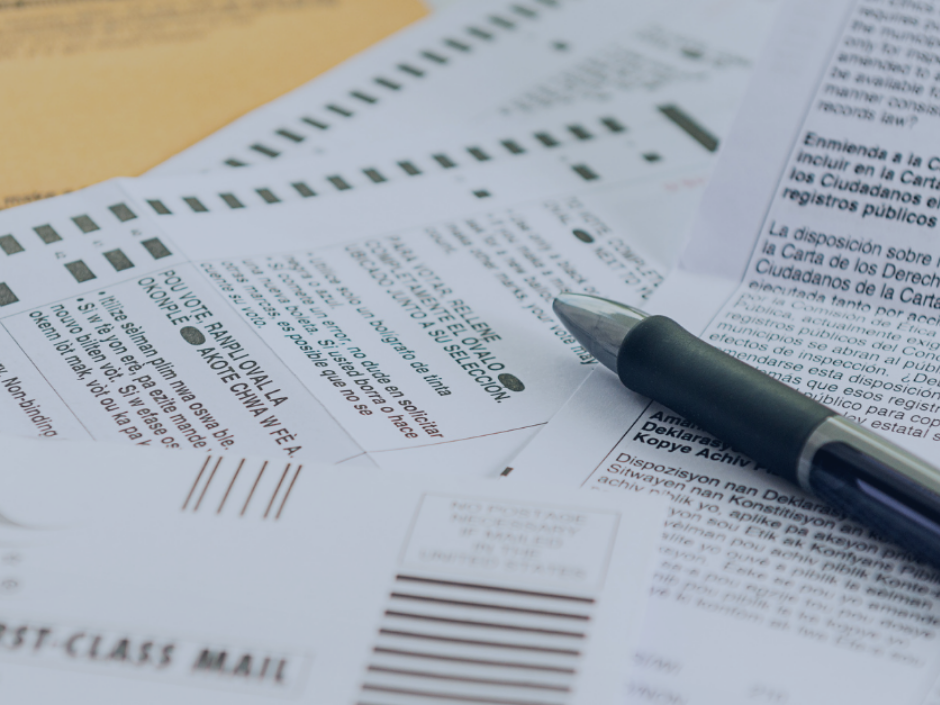 Several pages from a paper ballot piled on a desk, with a pen on top.