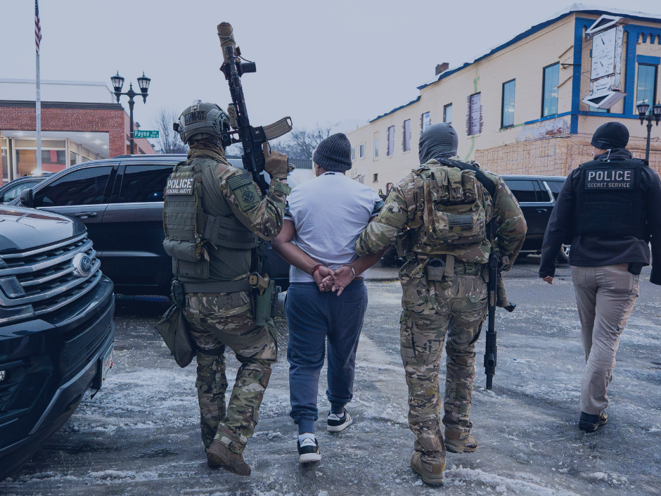 Image of ICE agents with guns arresting a person.