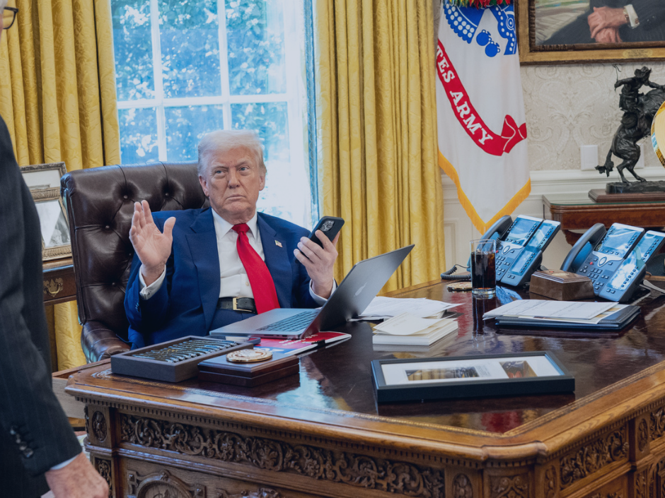 Image of President Donald Trump at his desk. Papers, a laptop, and a phone are on the desk.